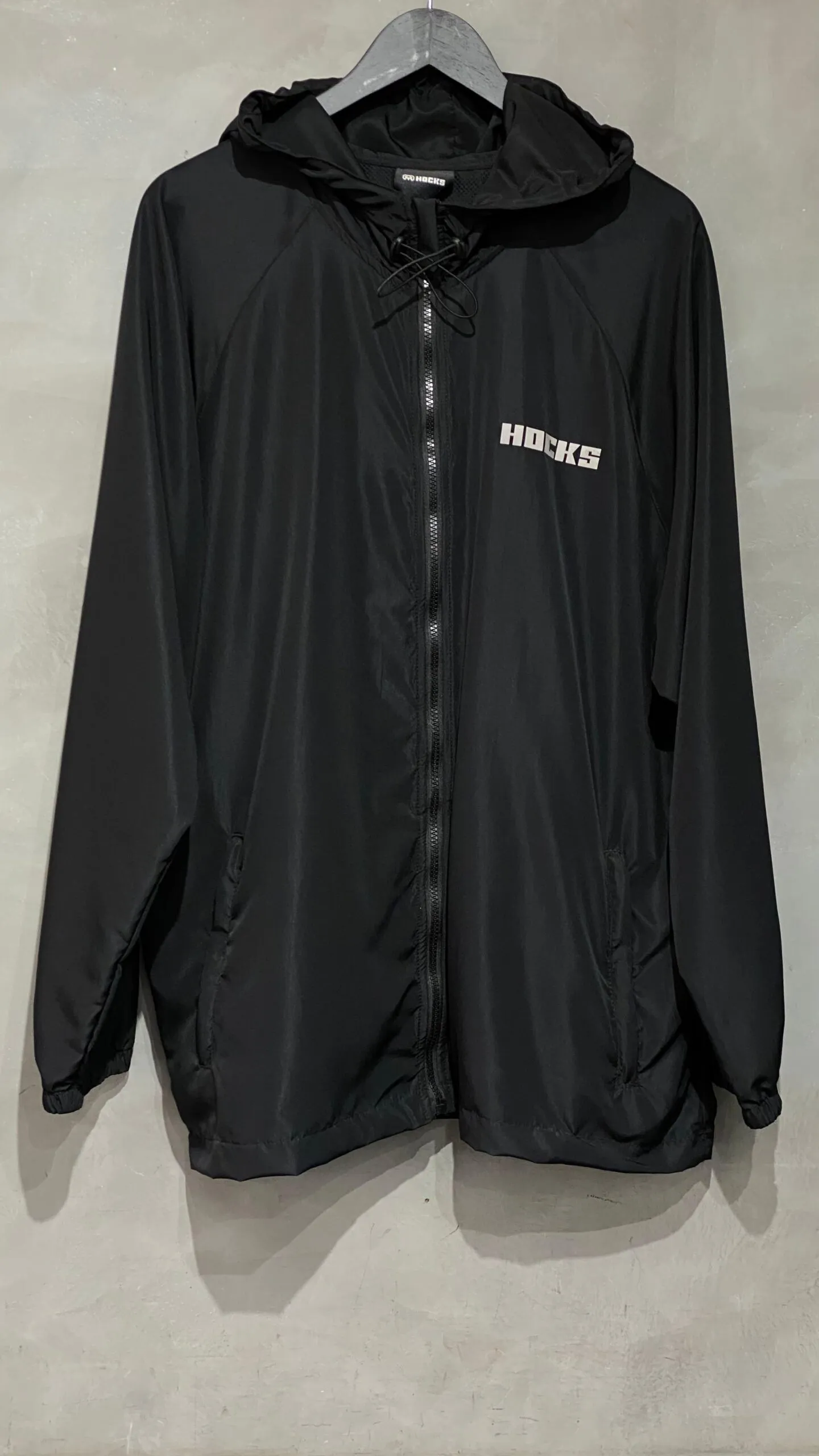 Jaqueta corta vento Hocks com logo refletivo na cor preta, ideal para proteção e estilo urbano.